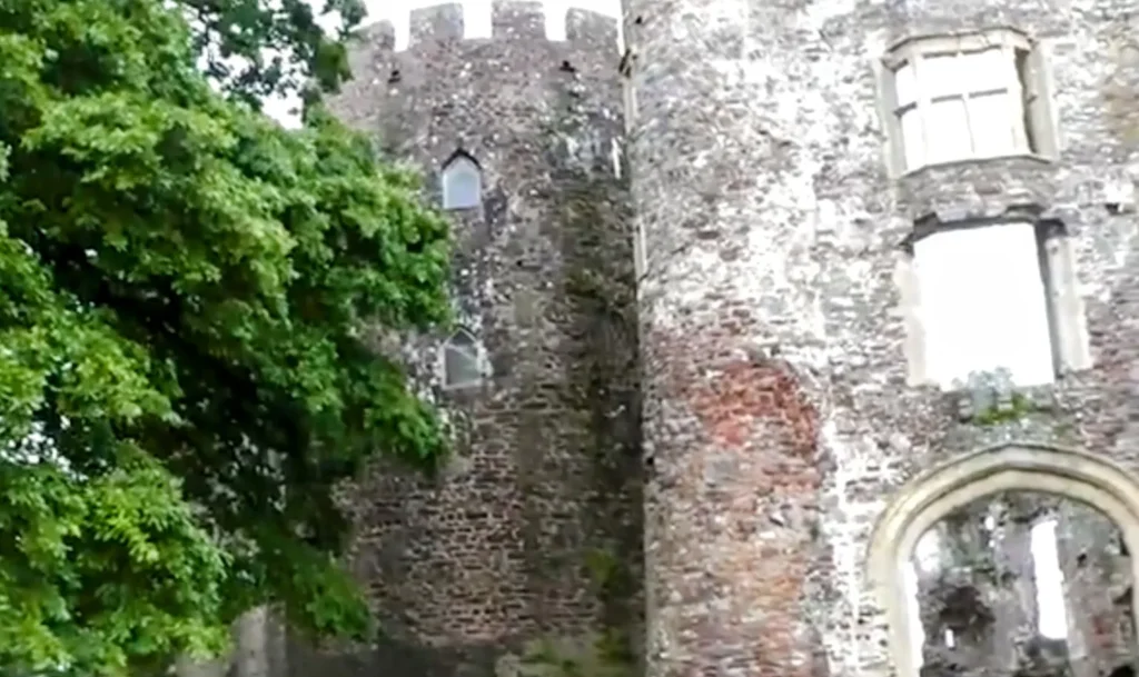 Close-up of a round tower at Laugharne Castle, with medieval stone walls partially covered by greenery and narrow arched windows.